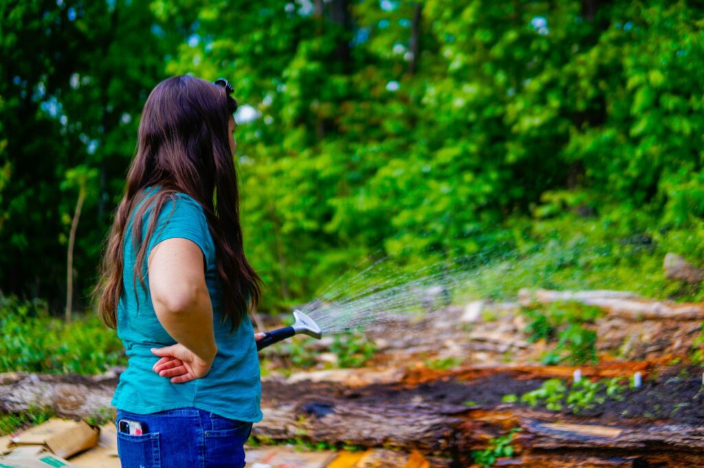 A woman watering plants in a garden with a hose.
