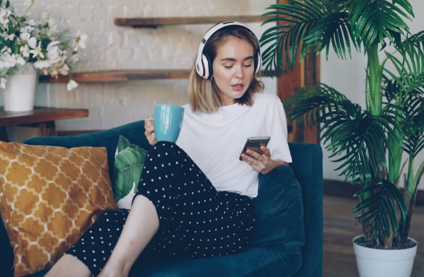 Woman listening to music on phone while holding mug.