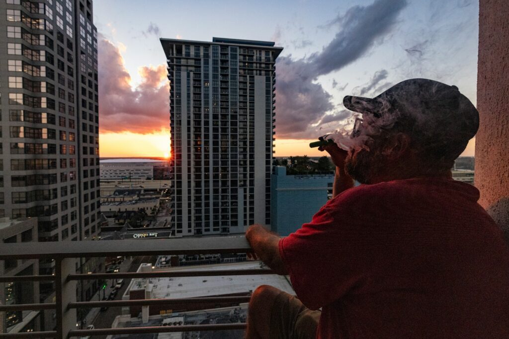 Man smoking cigar on balcony overlooking city at sunset