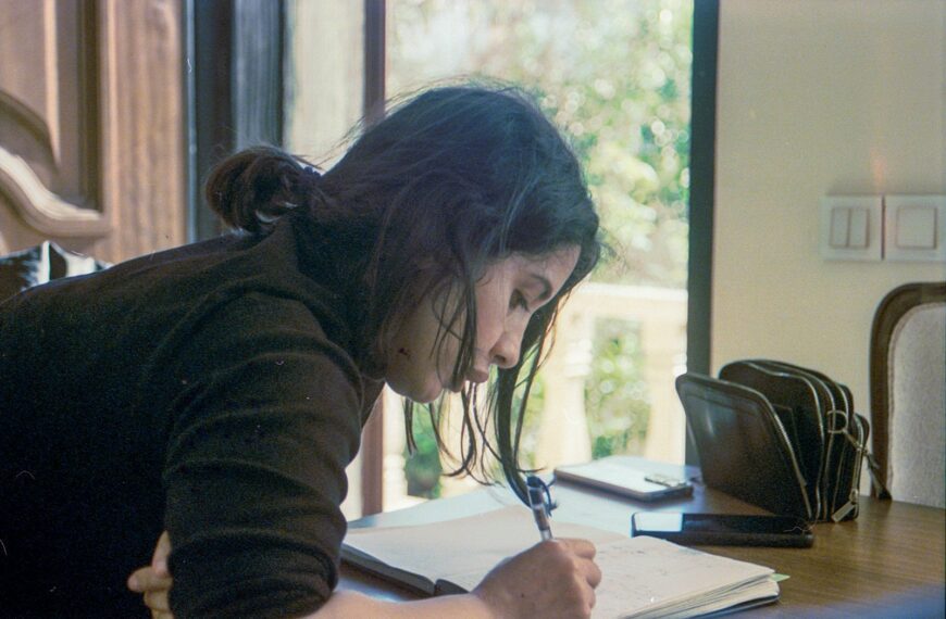 A woman writes in a notebook at a table.