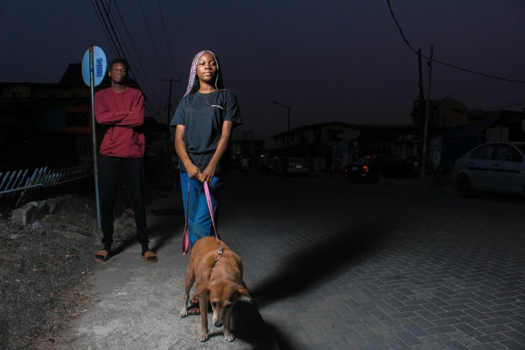 man in black t-shirt standing beside brown short coated dog during nighttime