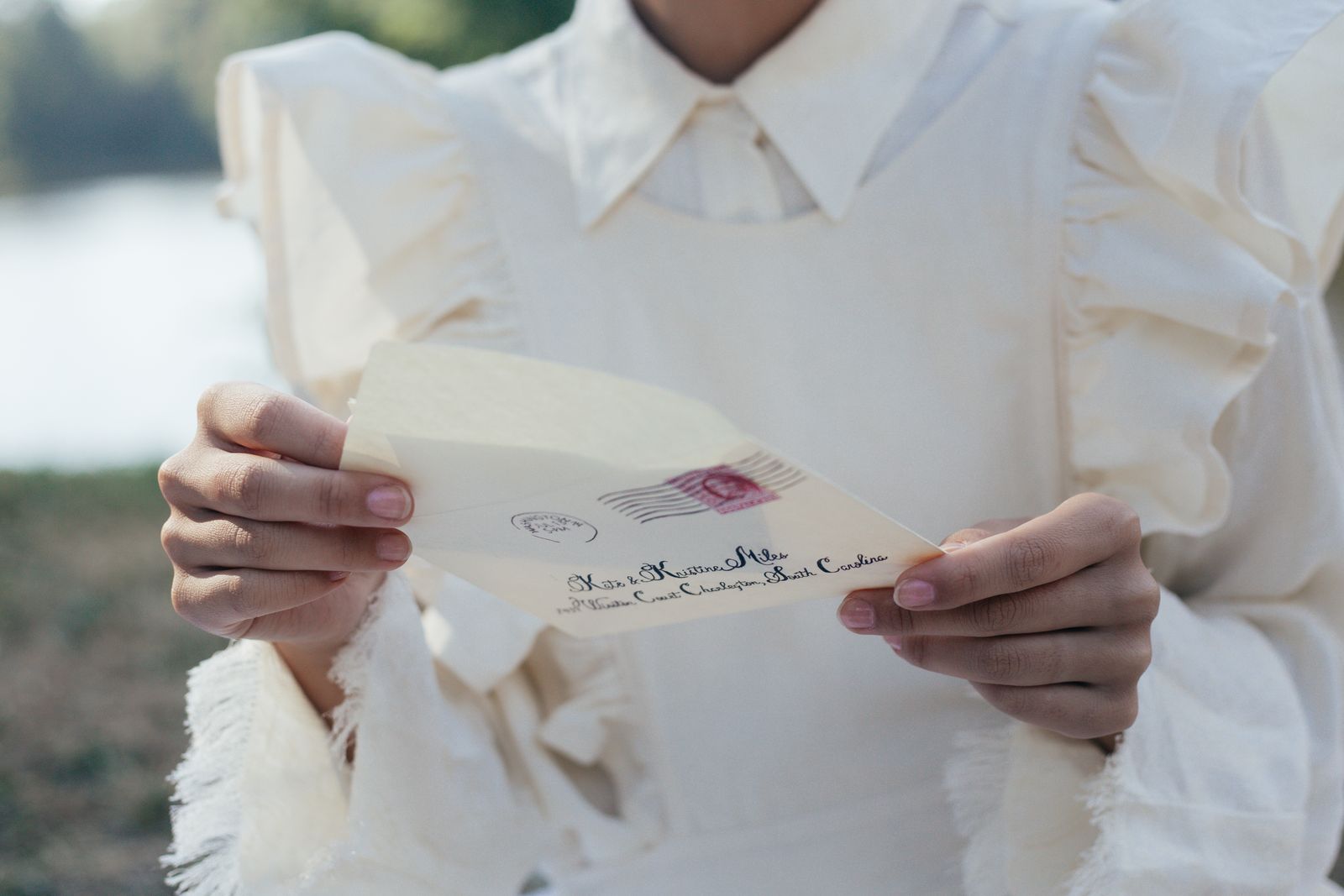 A woman in a white dress holds an old-fashioned love letter with serene background.