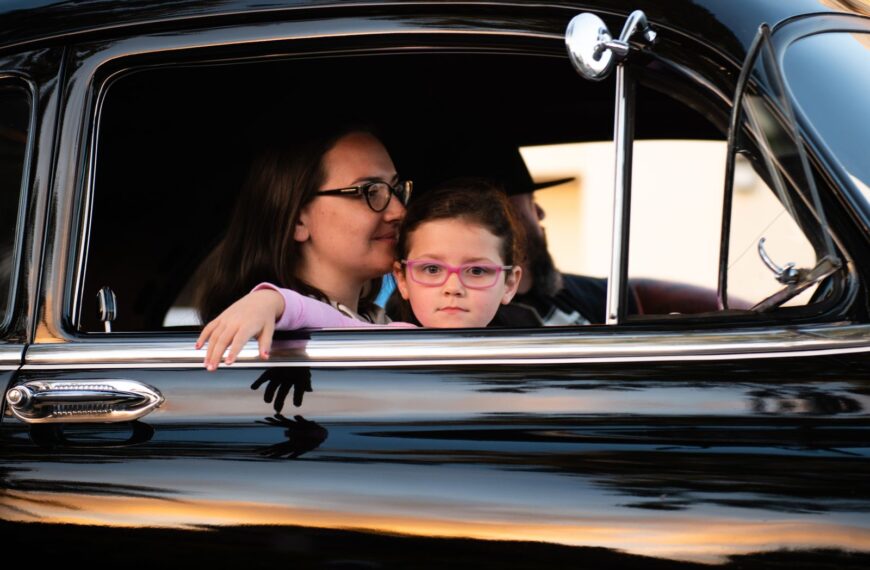 A mother and daughter enjoy a car ride in a vintage black automobile, capturing a serene family moment.