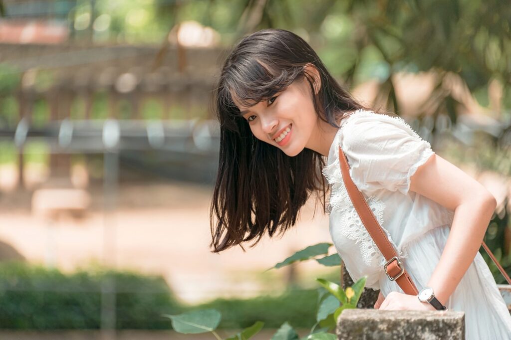 Charming young woman in a white dress smiling outdoors in a sunny park setting.