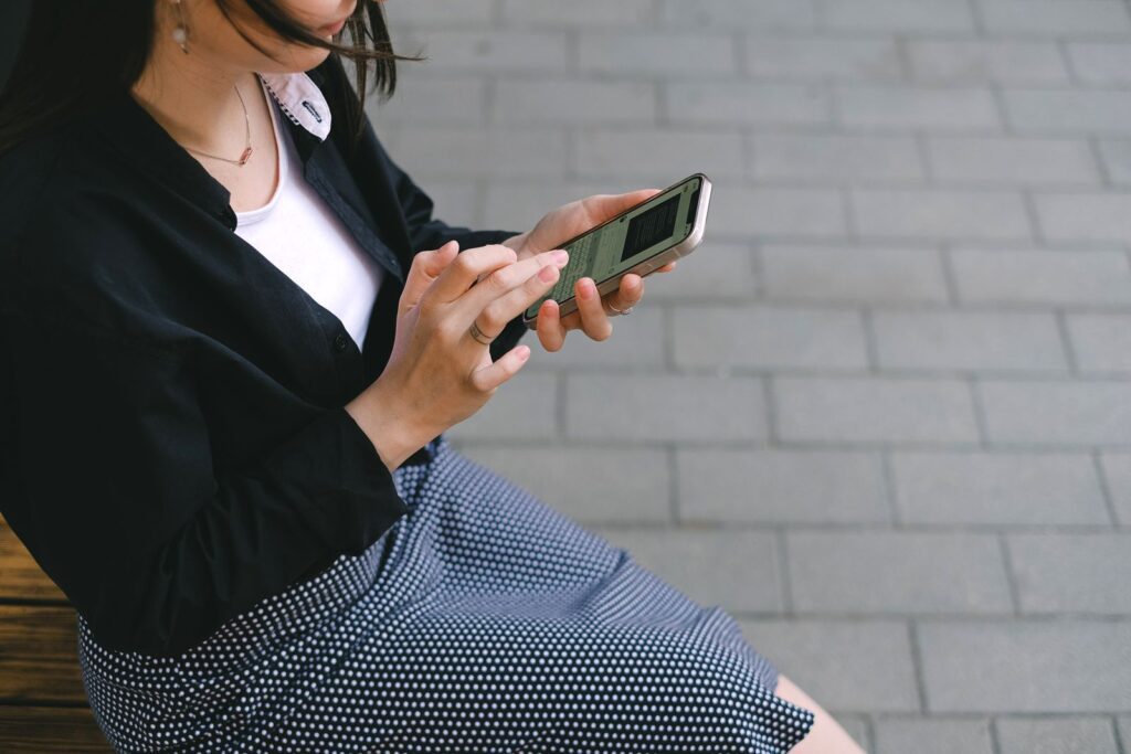 A woman using a smartphone outdoors in an urban setting, wearing a polka-dotted dress.