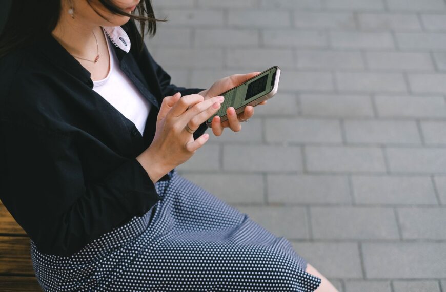 A woman using a smartphone outdoors in an urban setting, wearing a polka-dotted dress.