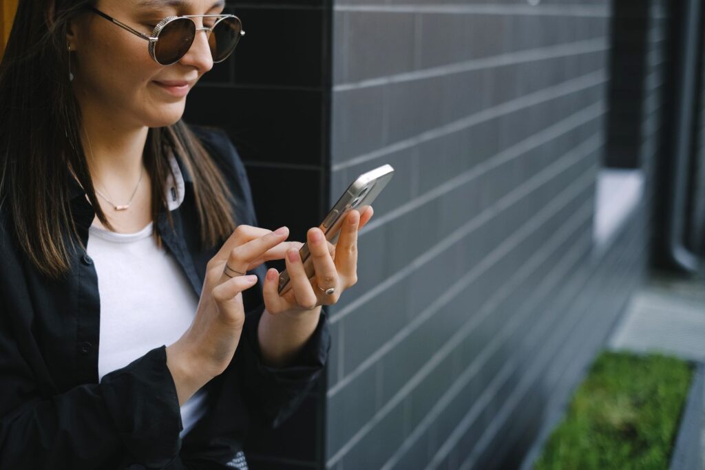 Confident young woman using smartphone outdoors by a modern building facade.