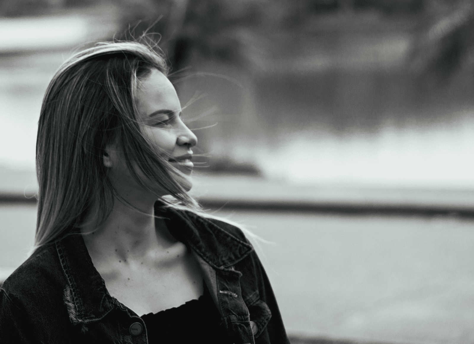 Captivating black and white portrait of a smiling woman in a denim jacket outdoors.