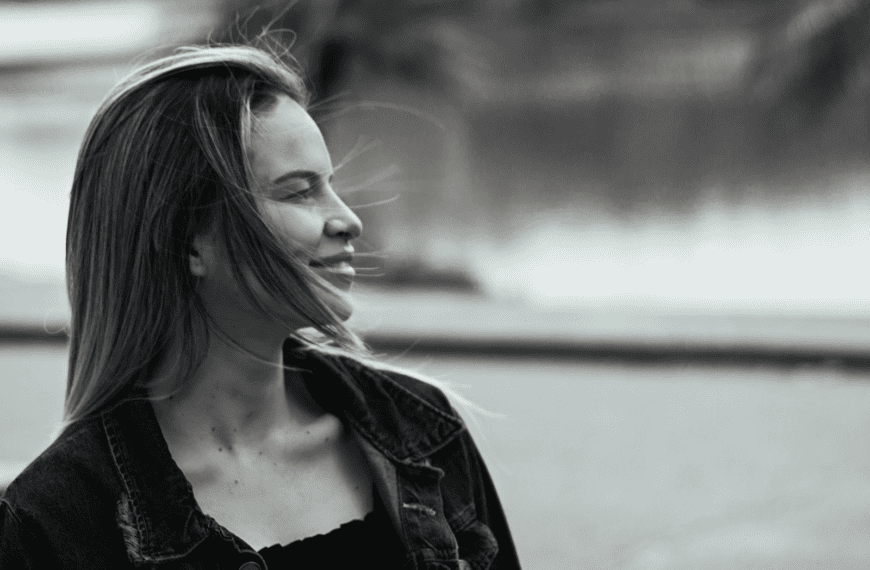 Captivating black and white portrait of a smiling woman in a denim jacket outdoors.