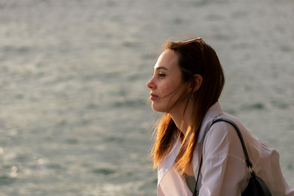 Side profile of a woman looking out to sea with a thoughtful expression during sunset.