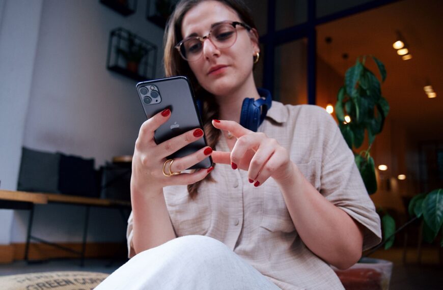 A young woman wearing eyeglasses uses a smartphone while relaxing in a modern café.
