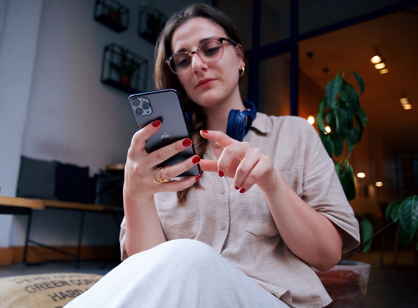 A young woman wearing eyeglasses uses a smartphone while relaxing in a modern café.