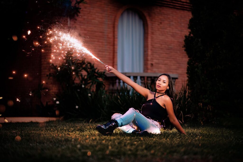 A young woman sits outdoors at night, celebrating with a sparkler, creating a festive atmosphere.