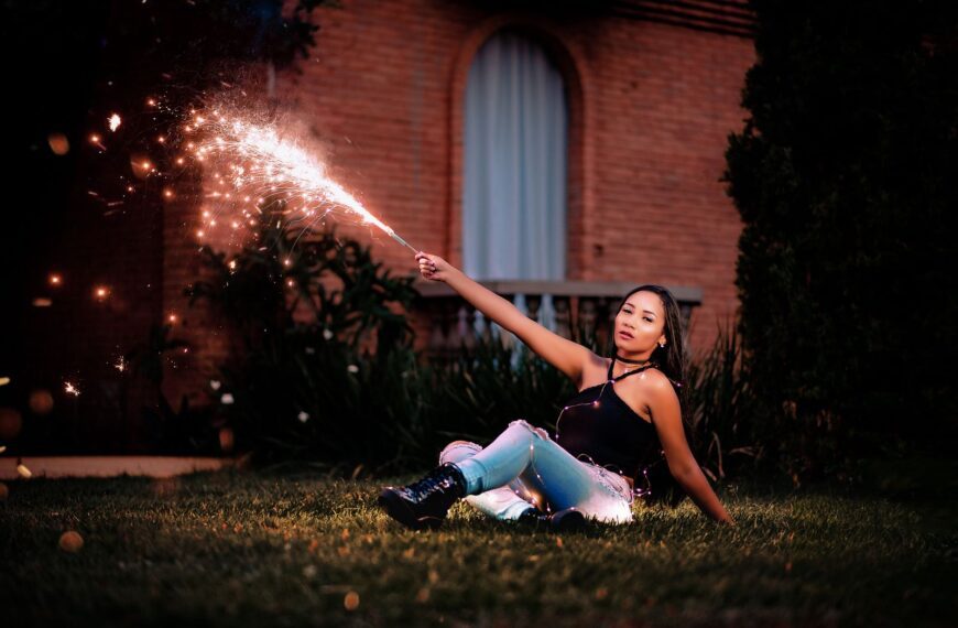A young woman sits outdoors at night, celebrating with a sparkler, creating a festive atmosphere.