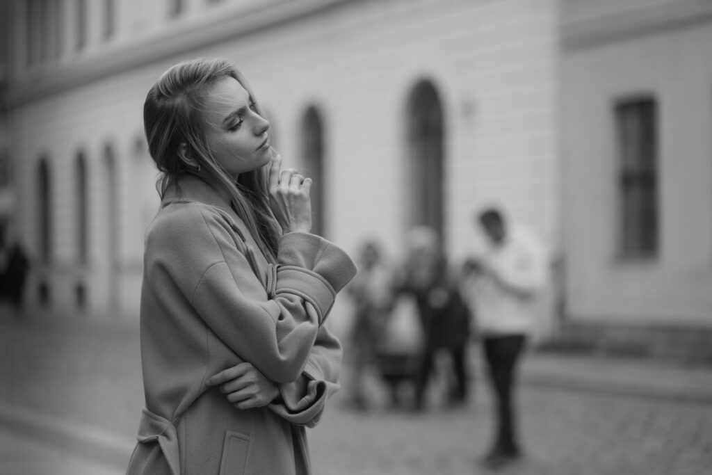 Black and white portrait of a thoughtful woman standing on a city street.