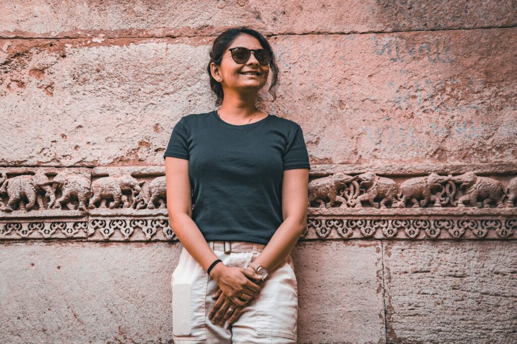 A woman in sunglasses smiles in front of a detailed ancient stone wall bas-relief.