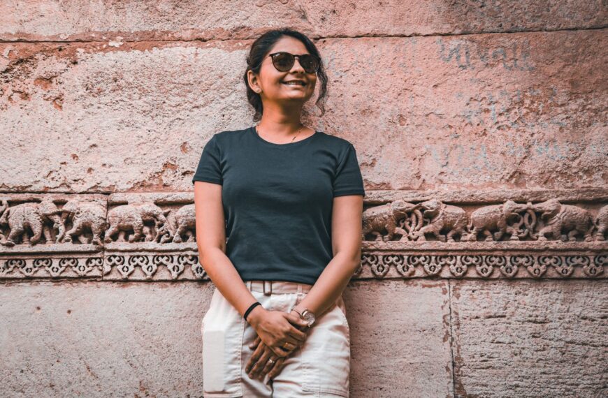 A woman in sunglasses smiles in front of a detailed ancient stone wall bas-relief.