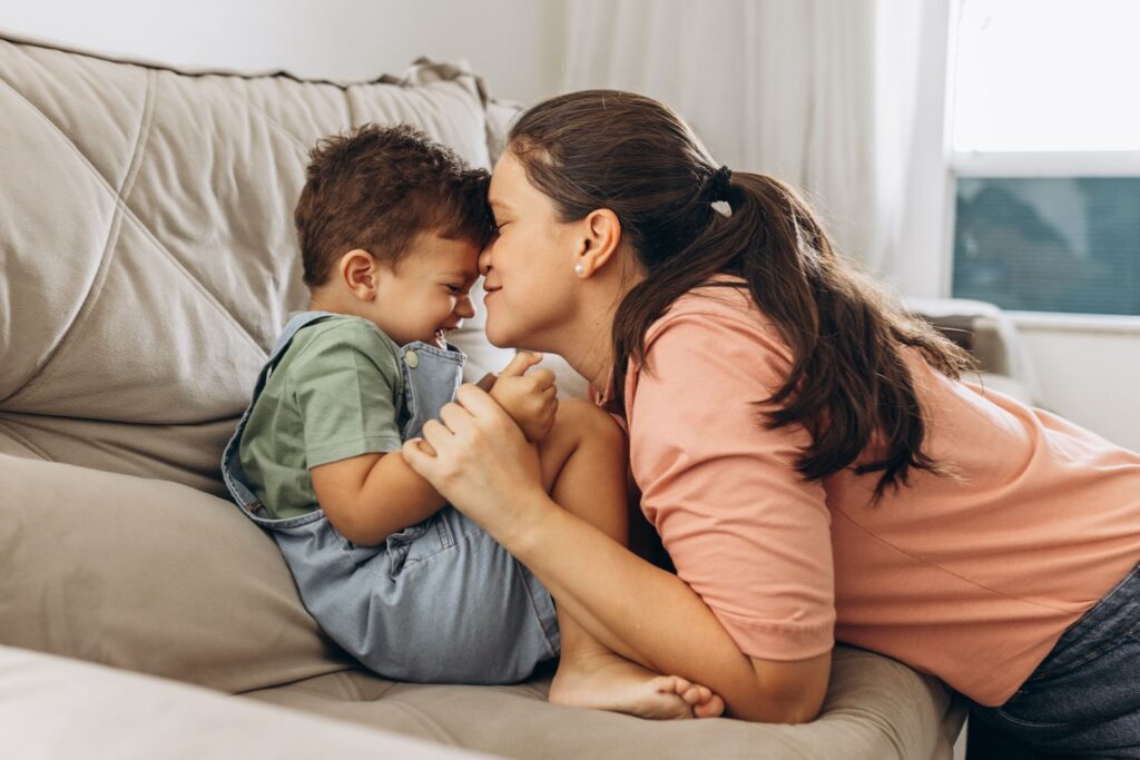 Mother and young son playfully bonding on the living room sofa, sharing a joyful moment.