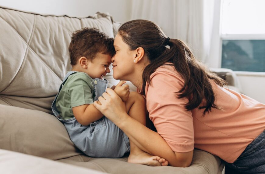 Mother and young son playfully bonding on the living room sofa, sharing a joyful moment.