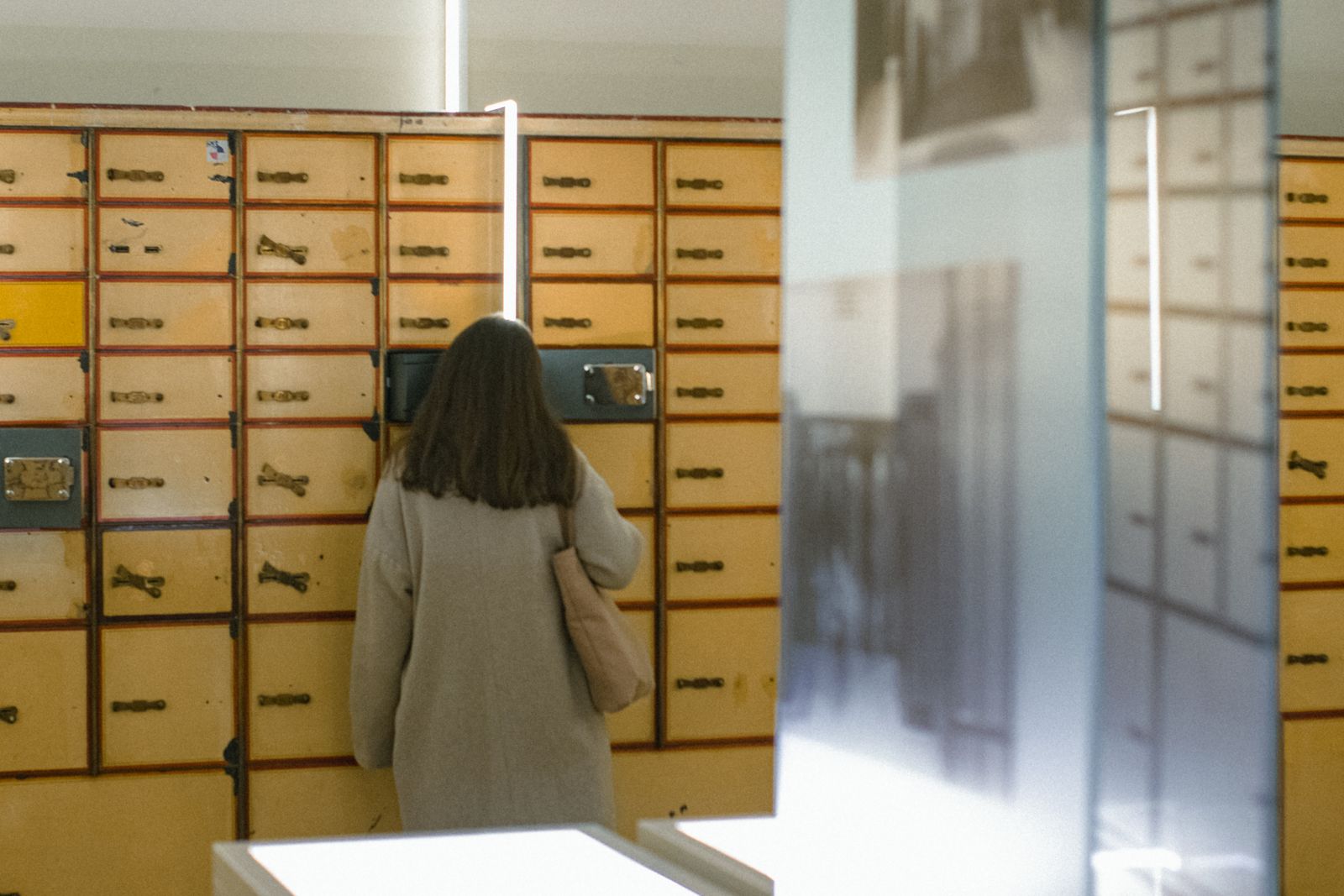 Woman with long brown hair looking at vintage mailboxes in an indoor setting.