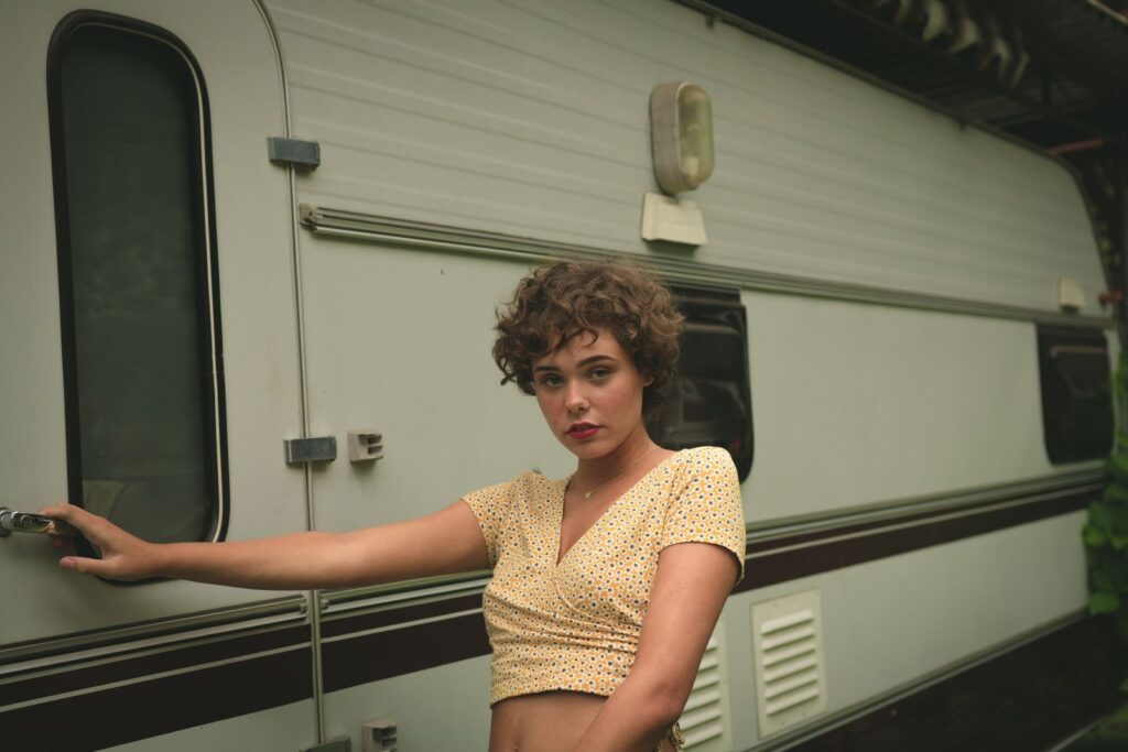 Young woman posing by a vintage trailer, exuding a casual and modern vibe.