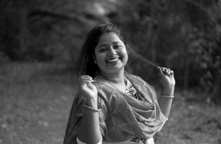 A joyful woman in traditional dress smiling in a rural outdoor setting.