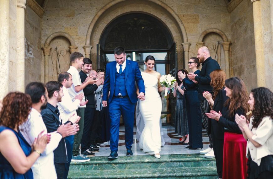 Bride and groom exiting a church, surrounded by applauding guests in an outdoor wedding ceremony.