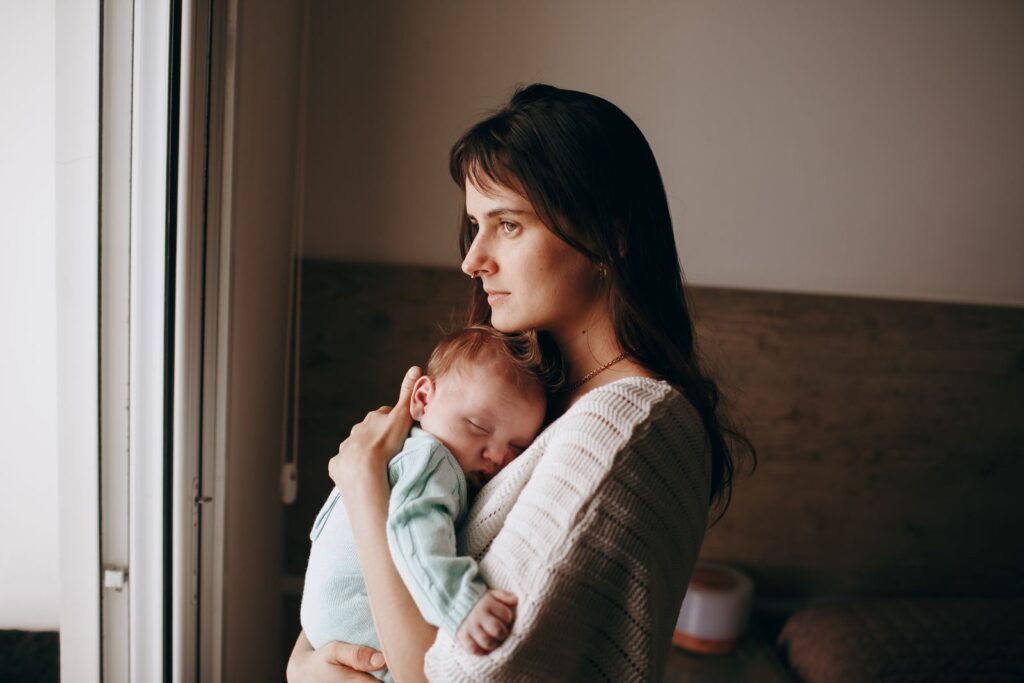 A serene moment of a mother holding her sleeping baby near a window, indoors.