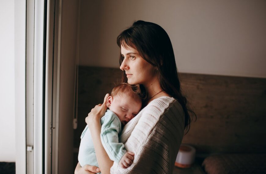 A serene moment of a mother holding her sleeping baby near a window, indoors.