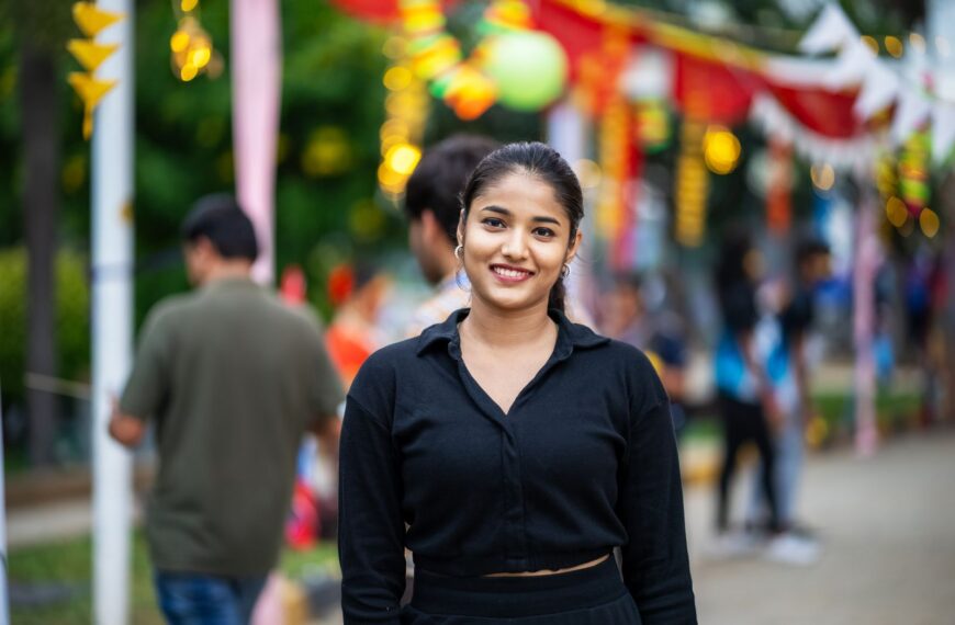 Young woman smiling at colorful outdoor street festival, celebrating a lively event.