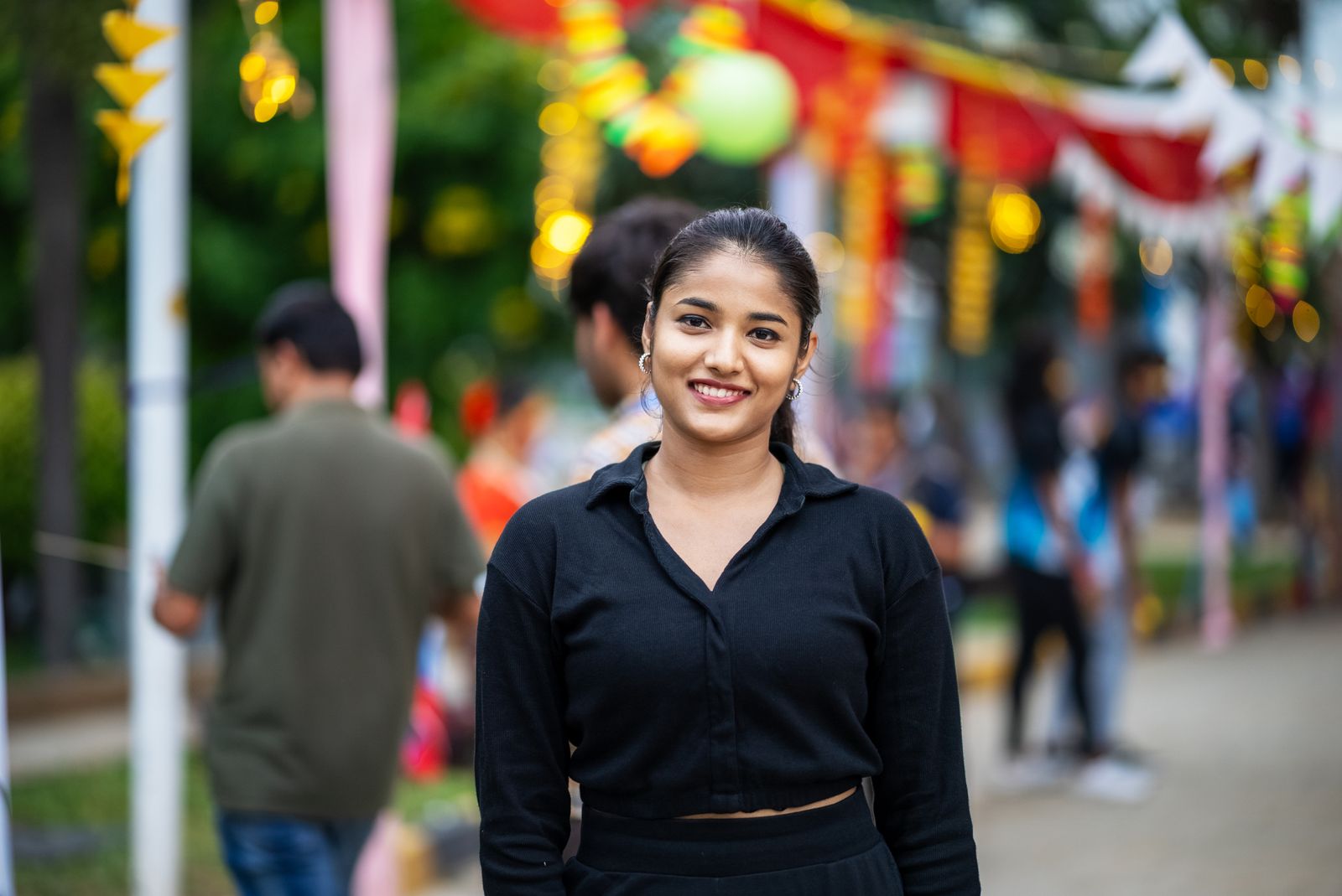 Young woman smiling at colorful outdoor street festival, celebrating a lively event.