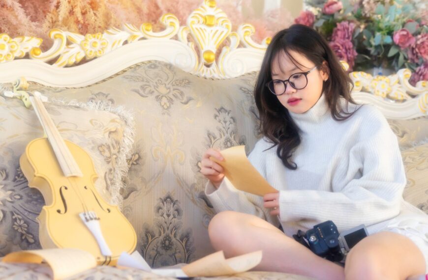 Woman in cozy sweater reading sheet music with violin on elegant sofa. Artistic ambiance.