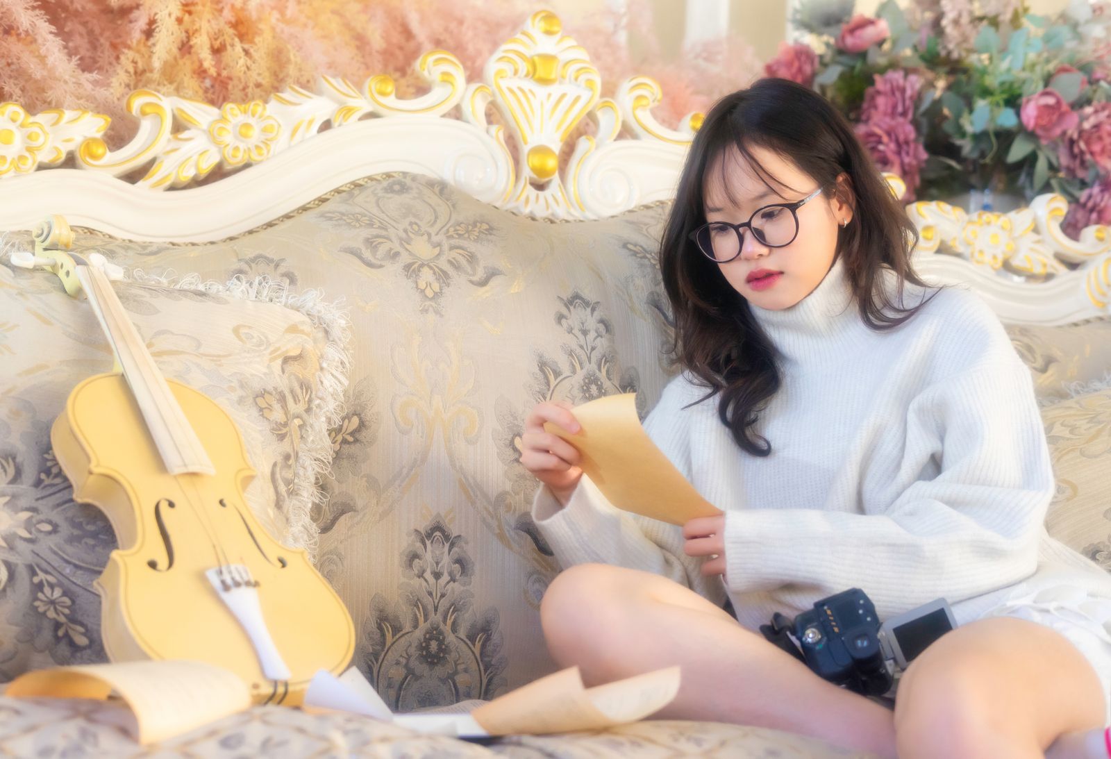 Woman in cozy sweater reading sheet music with violin on elegant sofa. Artistic ambiance.