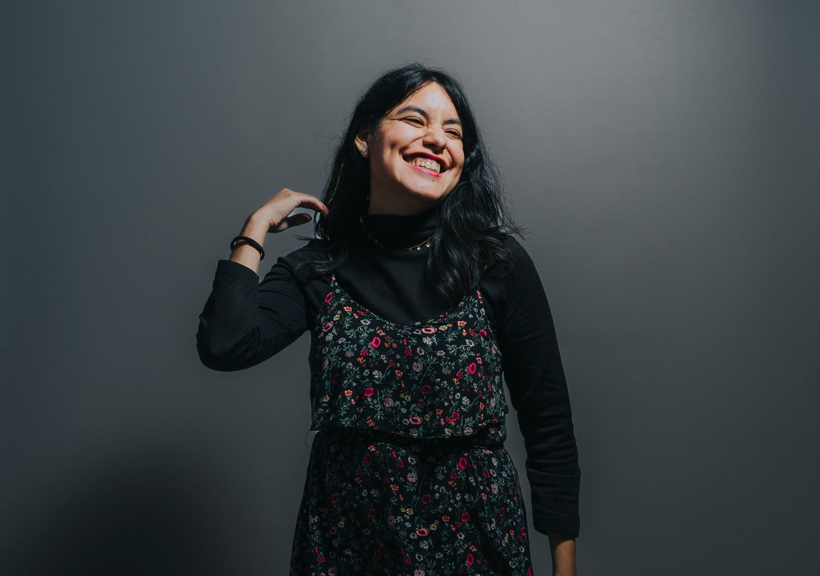 Smiling woman posing confidently in a floral dress against a grey background, exuding joy and positivity.