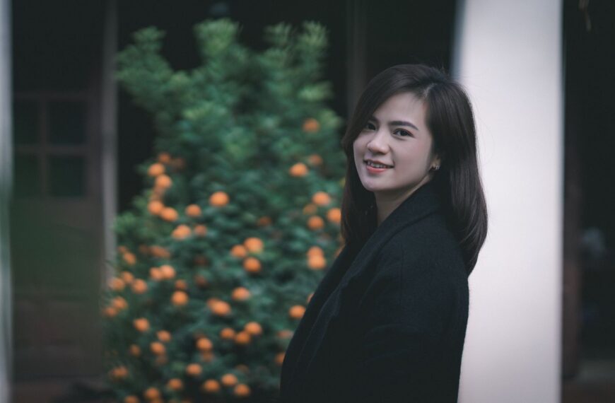 Charming portrait of a smiling woman standing outside near a tree.