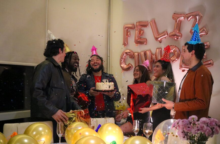 A joyful birthday party with friends, cake, and confetti indoors.