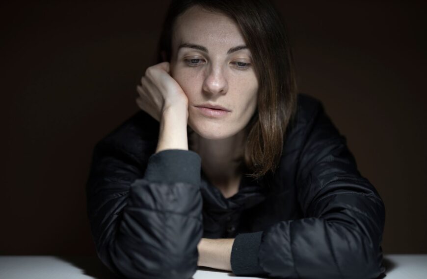 A woman in thought with a serious expression, indoors, in a low-light setting.