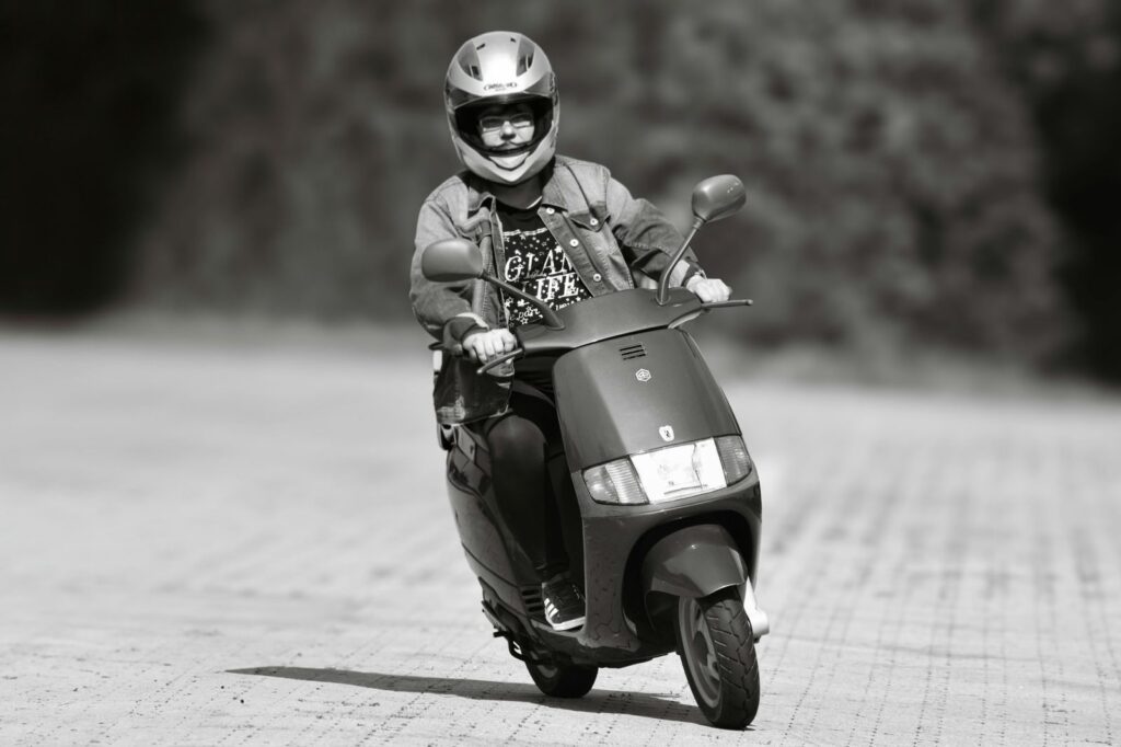 A person rides a scooter wearing protective gear on an outdoor path in black and white photo.