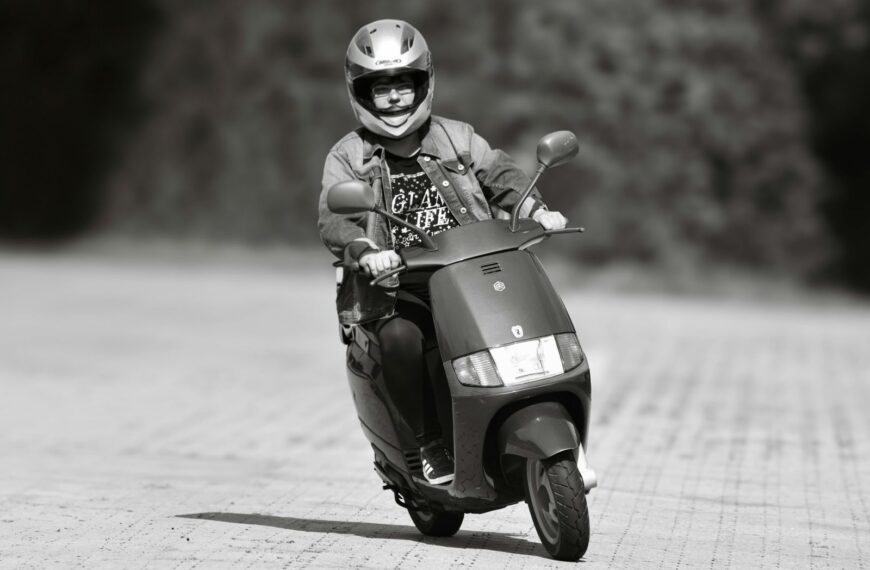 A person rides a scooter wearing protective gear on an outdoor path in black and white photo.