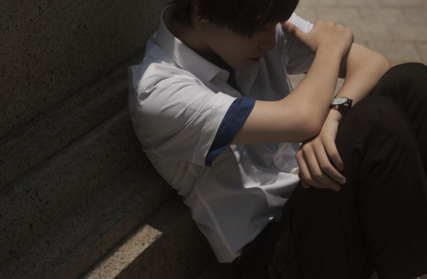 Teenager sitting thoughtfully on concrete steps, casting a shadow.