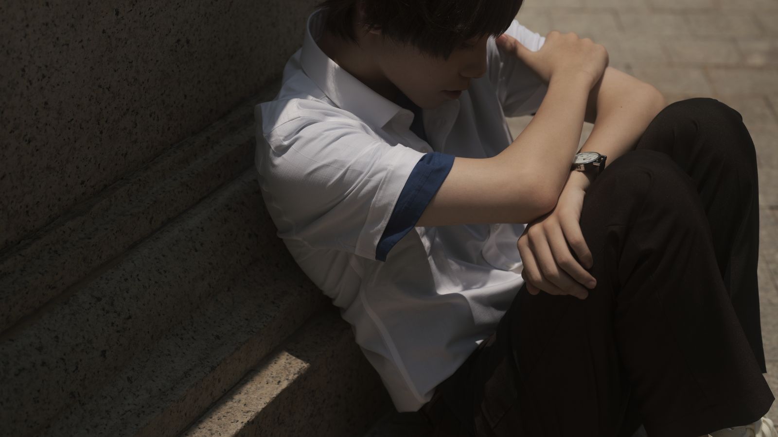 Teenager sitting thoughtfully on concrete steps, casting a shadow.