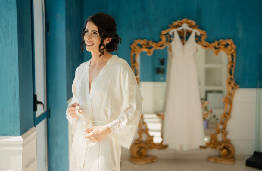 A bride enjoys a serene moment in a blue room with her wedding dress in the background.