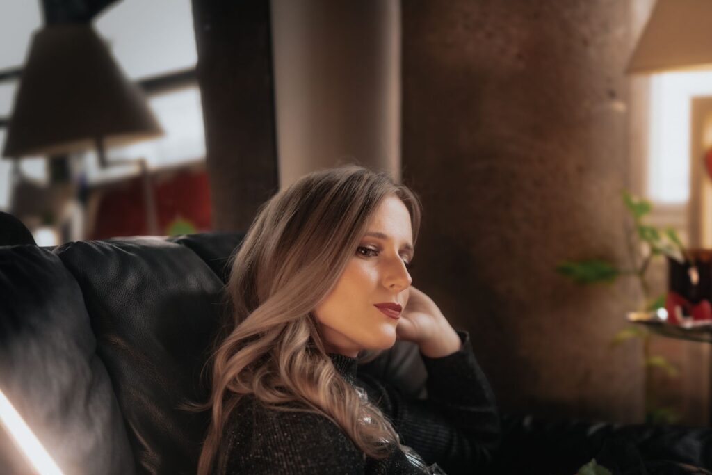 A thoughtful woman relaxing on a couch indoors with soft lighting.