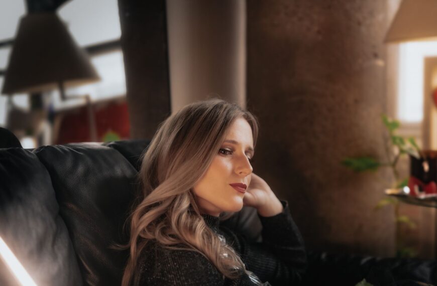 A thoughtful woman relaxing on a couch indoors with soft lighting.