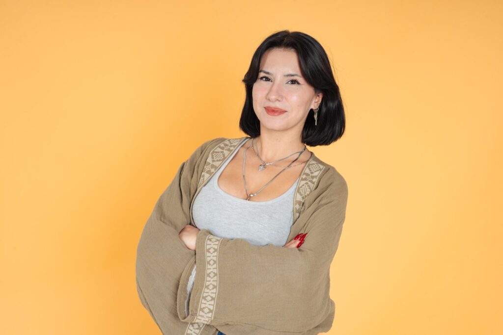 Confident woman with folded arms standing against a bright yellow background.