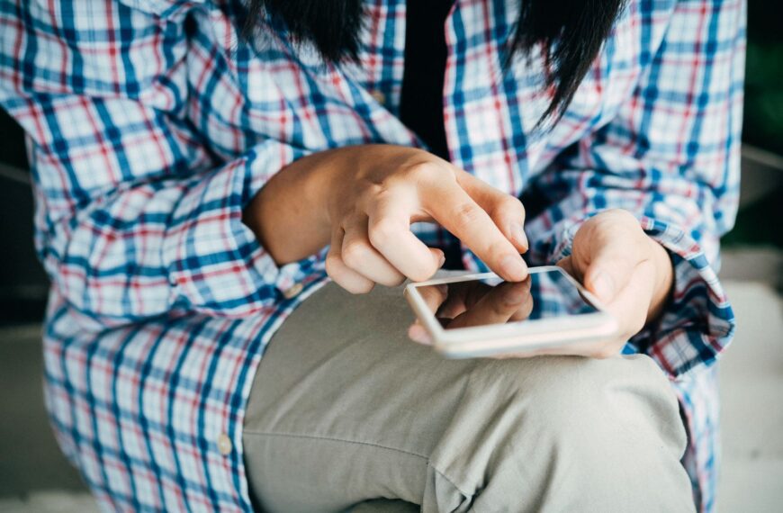 Woman's hands using a smartphone, wearing plaid shirt, indoors. Close-up shot highlighting touch interaction.