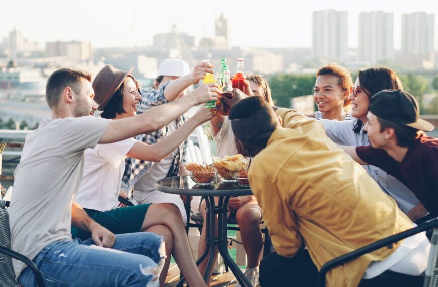 Diverse group of friends toasting with drinks on a sunny rooftop gathering.