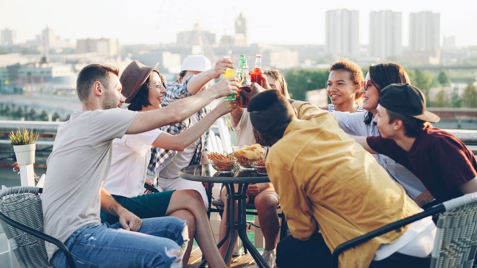 Diverse group of friends toasting with drinks on a sunny rooftop gathering.