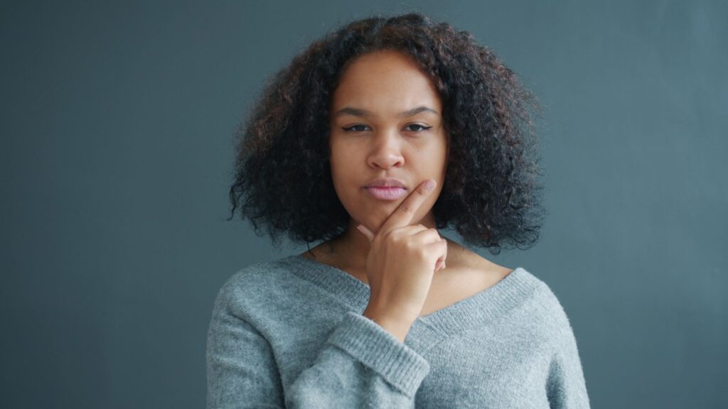A thoughtful woman in a gray sweater ponders deeply against a minimalist gray backdrop.