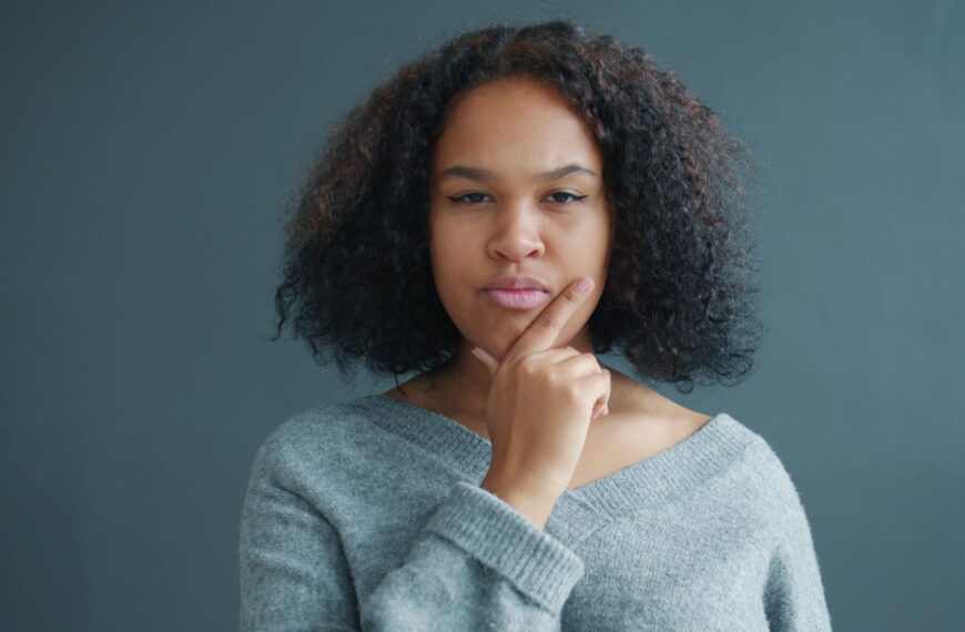 A thoughtful woman in a gray sweater ponders deeply against a minimalist gray backdrop.